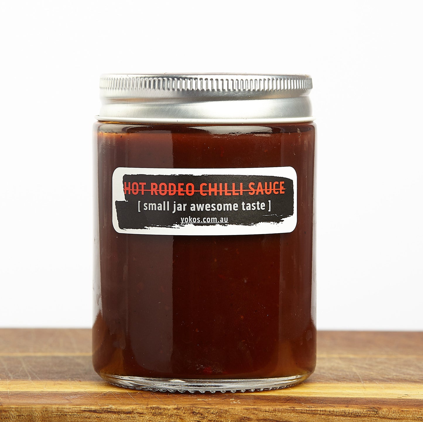 Jar of Byron Bay Hot Rodeo Chilli Sauce, gluten free and vegan, on a wooden surface with a white background. This sauce looks yummy!