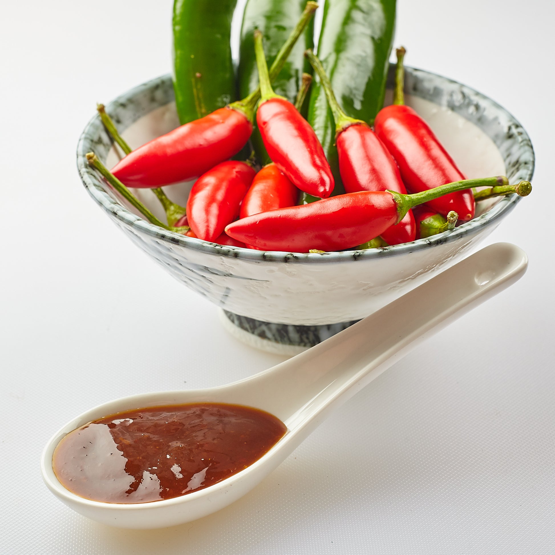 Yoko's Byron Bay Hot Rodeo Chilli sauce in a spoon with fresh birds eye chillis in a bowl. HOT!